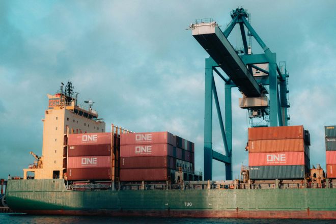 Large cargo ship loaded with colorful containers at a bustling industrial port.