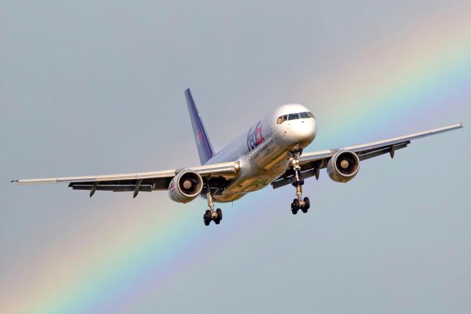 A cargo airplane in flight with a vivid rainbow in the background, showcasing a unique aerial view.