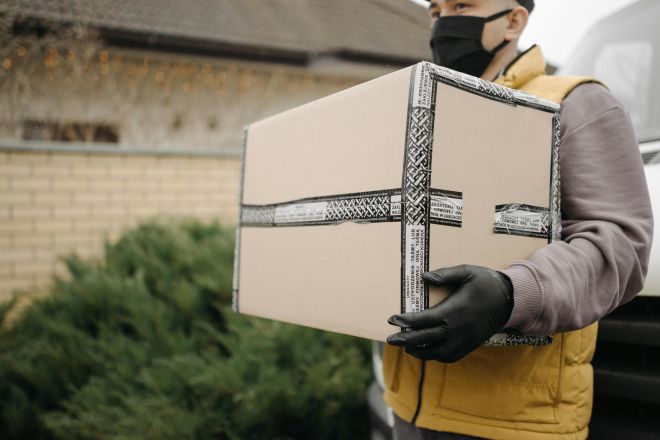Courier with mask and gloves delivering a package outdoors, embracing the new normal.
